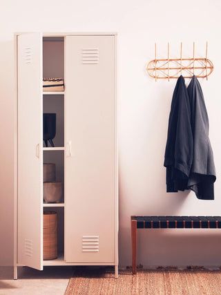 The CHOICEWARDROBE Ruston White Metal Locker Wardrobe (2 Door) with shelves and hanging rail is open, showcasing industrial storage next to a wall-mounted coat rack, a bench, and a woven rug on the floor.