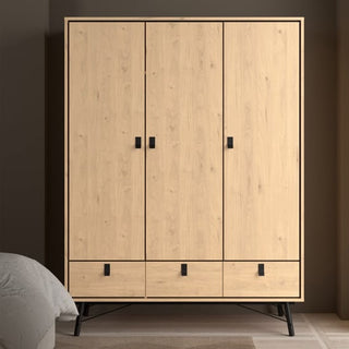 The CHOICEWARDROBE Rynok 150 cm 3 Door 3 Drawer Wardrobe in Jackson Hickory Oak features an industrial-Scandi design, black metal legs, and modern storage, ideal for a beige-walled room with a bed partially visible on the left.