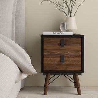 The CHOICEWARDROBE Rynok 3 Piece Wooden Bedroom Furniture Set in Walnut & Black includes a 3 door wardrobe, chest of drawers, and bedside table. The table holds the book POLLOCK, a glass of water, and a cream vase with branches against a beige wall.