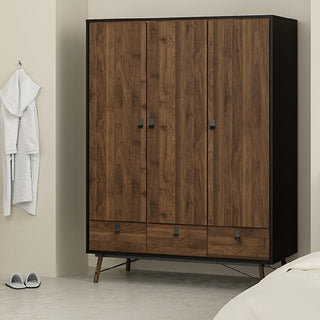 The CHOICEWARDROBE Rynok 3 Piece Wooden Bedroom Furniture Set in walnut & black features a 3-door wardrobe with lower drawers, chest of drawers, and bedside table, shown here against a beige wall with a white robe and slippers nearby.