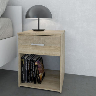 The CHOICEWARDROBE Scalia Oak Bedside Table from the 3 Piece Collection features a single drawer and open shelf, topped with a modern black lamp, placed next to a white-bedded bed against a light gray wall.