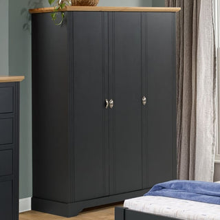 The CHOICEWARDROBE Talox 3 Door Wardrobe in grey with an oak top, classic country style, stands against a green wall near a window with gray curtains. A matching dresser and bed with blue bedding complete the cozy look.