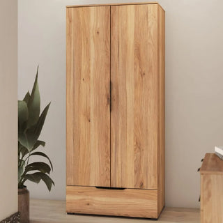 The CHOICEWARDROBE Tarzana 2 Door Wardrobe with Bottom Drawer in Mauvella Oak (86cm wide) stands against a beige wall, ideal for bedroom storage, with a green plant on the left and part of a wooden table to the right.