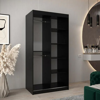 The CHOICEWARDROBE Tavira 100cm Black 2 Door Sliding Wardrobe with shelves and a hanging rail stands in a modern room with light wood flooring, striped panels, a round mirror, green sofa, and pampas grass vase.