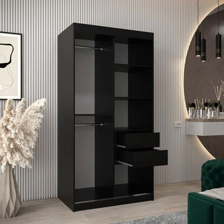 The CHOICEWARDROBE Tavira 100cm Black 2 Door Sliding Wardrobe with shelves and a hanging rail stands in a modern room with striped walls, decorative lighting, a green chair, and a vase of pampas grass.