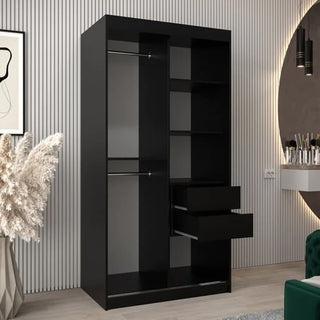 The CHOICEWARDROBE Tavira 100cm Black Mirrored Sliding Door Wardrobe, featuring a modern compact design with a hanging rail and storage shelves, stands in a stylish room with a slatted wall, pampas grass, vanity table, and wall mirror.