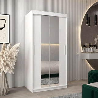 The CHOICEWARDROBE Tavira 100cm White Mirrored Sliding Door Wardrobe, featuring a compact modern design with internal shelves and smooth glide doors, stands in a stylish bedroom with vertical wall panels, pendant lights, pampas grass, and a round mirror.