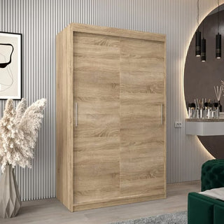 The CHOICEWARDROBE Tavira 120cm Sonoma Oak Sliding Door Wardrobe, featuring smooth sliding panels and smart storage, stands in a modern room with light wood flooring, mirror, pendant lights, green velvet sofa, white vanity table, and minimalist decor.
