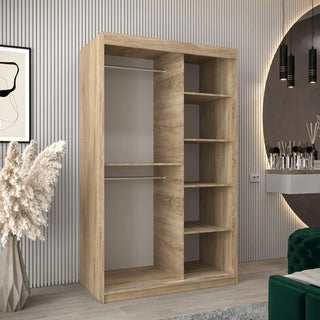 The CHOICEWARDROBE Tavira 120cm Sonoma Oak Sliding Door Wardrobe offers smart bedroom storage with space-saving 2-door sliding panels, ideal for modern rooms featuring gray walls, a green chair, and stylish decorative accents.