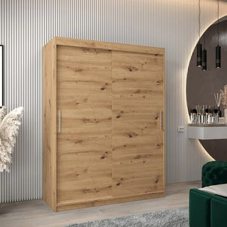 The CHOICEWARDROBE Tavira 150 cm Artisan Oak Sliding Door Wardrobe, featuring a modern 2-door design and natural wood finish, offers stylish bedroom storage against a grooved wall, complemented by pampas grass and a vanity with mirror.