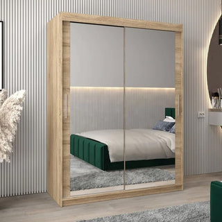 The CHOICEWARDROBE Tavira 150cm Sonoma Oak Mirrored Sliding Door Wardrobe features a compact 2-door design with full-length mirrors, complementing a modern bedroom with a green upholstered bed, gray rug, and neutral vertical-lined walls.