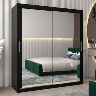 A CHOICEWARDROBE Tavira 180cm Black Mirrored Sliding Door Wardrobe with full-length mirrors reflects a modern bedroom with a green upholstered bed, grey carpet, vertical-line wall accents, and ambient lighting.