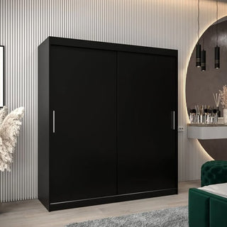 A modern bedroom showcases the CHOICEWARDROBE Tavira 180cm Black Sliding Door Wardrobe with silver handles, set against vertical white paneling and placed beside a round mirror and decorative accents.