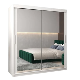 The CHOICEWARDROBE Tavira 180cm White Mirrored Sliding Door Wardrobe, with full-length mirrors and a bright minimalist design, reflects a stylish bedroom with a green upholstered bed, gray rug, and vertical panel wall with strip lighting.