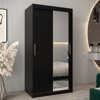A CHOICEWARDROBE Tavira 2 Door Sliding Mirrored Wardrobe in sleek black, featuring a full-length mirror panel and spacious shelves, sits in a modern bedroom with striped wall paneling, reflecting the bed and décor accents.