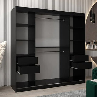 The CHOICEWARDROBE Tavira 2 Door Sliding Mirrored Wardrobe in black matte finish with full-length mirrors, a hanging rail, and shelves stands against a white paneled wall. A green chair and vanity are on the right side.
