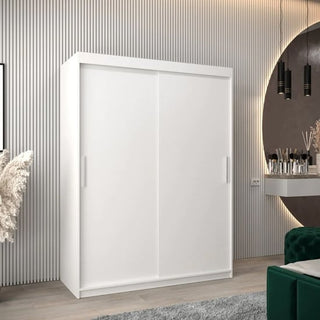A CHOICEWARDROBE Tavira 2 Door Sliding Wardrobe (150cm, Matt White) with shelves and drawers stands against a grooved wall. Nearby are a round mirror, pendant lights, vanity table, green velvet chair, and pampas grass in a vase.