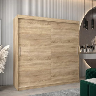 The CHOICEWARDROBE Tavira 2 Door Sliding Wardrobe in a 200 cm Sonoma Oak finish stands against paneled walls. Beside it, a vanity table with mirror, makeup items, and two pendant lights completes the modern setup.