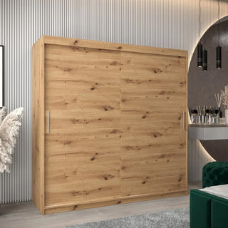 A CHOICEWARDROBE Tavira 2 Door Sliding Wardrobe in 200cm Artisan Oak finish, featuring shelves, drawers, and hanging rails, stands by a paneled wall. A vanity table with a mirror and decor appears on the right.