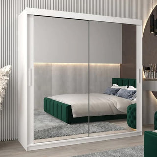 A modern bedroom features the CHOICEWARDROBE Tavira 200cm White Mirrored Sliding Door Wardrobe, reflecting a green upholstered bed, gray rug, and striped wall paneling in soothing neutral and green tones.