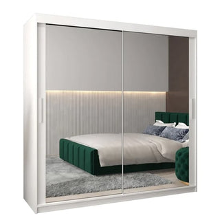 The CHOICEWARDROBE Tavira 200cm White Mirrored Sliding Door Wardrobe reflects a bedroom with a green upholstered bed, gray rug, pillows, and a softly lit accent wall with vertical paneling.