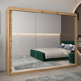 The CHOICEWARDROBE Tavira 250cm Sonoma Oak wardrobe with mirrored sliding doors reflects a modern bedroom with a green upholstered bed, gray rug, and neutral vertical-lined walls.