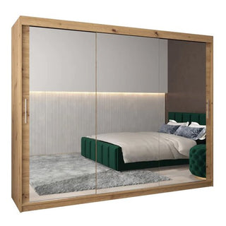 The CHOICEWARDROBE Tavira 250cm Mirrored Sliding Door Wardrobe in Sonoma Oak features 3 doors with full-length mirrors, complementing a modern bedroom with a green upholstered bed, gray rug, and textured wall with horizontal lighting.