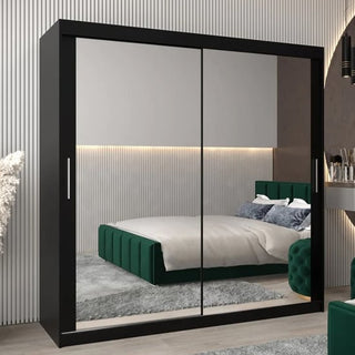 The CHOICEWARDROBE Tavira 250cm Sonoma Oak Mirrored Sliding Door Wardrobe with a modern 3-door design and full-length mirrors reflects a bedroom featuring a green upholstered bed, gray rug, and light-striped walls.