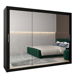 The CHOICEWARDROBE Tavira 3 Door Mirrored Sliding Wardrobe in black features full mirror panels and complements a modern bedroom with a green upholstered bed, gray rug, white bedding, and vertical panel light walls.