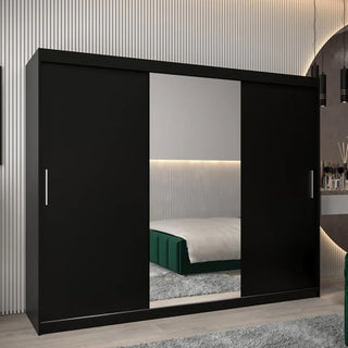 The CHOICEWARDROBE Tavira 3 Door Sliding Mirrored Wardrobe in black (250cm extra-wide, central mirror, deep storage, adjustable shelving) stands in a modern bedroom, reflecting the bed and part of a dresser.