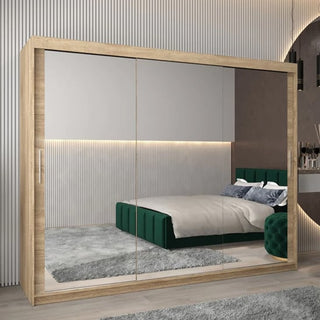 The CHOICEWARDROBE Tavira 3 Door Sliding Mirrored Wardrobe in Oak Finish (250cm wide) stands in a modern bedroom, reflecting a green-headboard bed, gray rug, and vertical wall paneling with its full-length mirrors and sleek design.