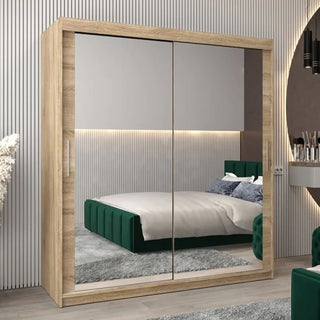 A modern bedroom with the CHOICEWARDROBE Tavira 3 Door Sliding Mirrored Wardrobe in Sonoma Oak finish, featuring full-length mirror panels. The reflection reveals a green upholstered bed, gray rug, and LED-lit wall section.
