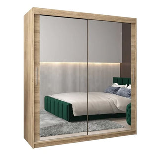 The CHOICEWARDROBE Tavira 3 Door Sliding Mirrored Wardrobe in Sonoma Oak finish (180cm) reflects a modern bedroom with a green bed, gray carpet, and an accent wall with vertical lines and LED lighting.