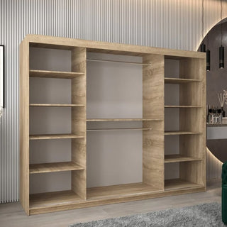 The CHOICEWARDROBE Tavira 3 Door Sliding Wardrobe in Sonoma Oak (250cm) with internal shelving and smooth sliding doors stands by a wall with vertical grooves; a round mirror and modern pendant lights appear on the right.