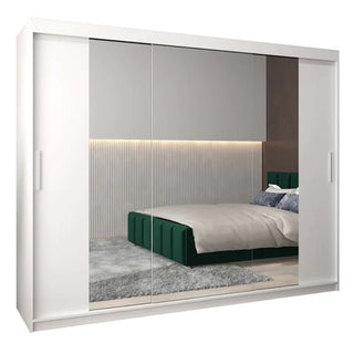 The CHOICEWARDROBE Tavira II 3 Door Mirrored Sliding Wardrobe in white (250cm, full mirror panels) reflects a modern bedroom with a green upholstered bed, gray rug, and ribbed wall paneling with warm lighting.