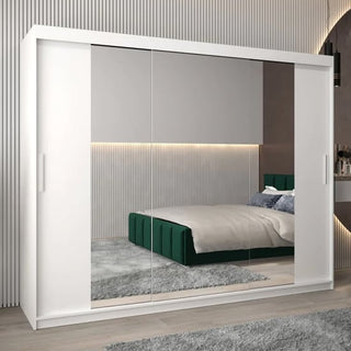 A modern bedroom features the CHOICEWARDROBE Tavira II 3 Door Mirrored Sliding Wardrobe in a white finish (250cm wide, full mirror panels), reflecting a green upholstered bed, grey rug, and minimalist neutral decor with accent lighting.