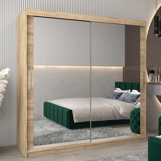 The CHOICEWARDROBE Tavira Mirrored Sliding Door Wardrobe 200cm in Sonoma Oak features two full-length mirrored doors and spacious shelves, perfectly reflecting a modern room with a green bed, gray rug, and light vertical-lined walls.