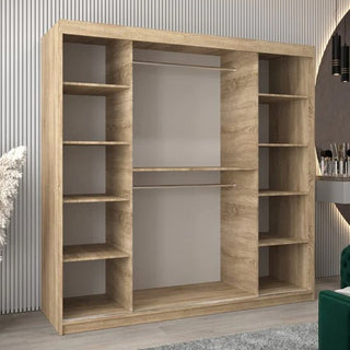 The CHOICEWARDROBE Tavira Mirrored Sliding Door Wardrobe in Sonoma Oak stands on a light floor beside vertical paneling, with a nearby green chair and vanity from Furniture in Fashion partially visible.