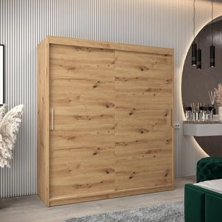The CHOICEWARDROBE Tavira Wardrobe 180cm in artisan oak finish stands against a paneled wall. With 2 sliding doors, spacious shelving, and hanging storage, it offers stylish bedroom organization. Modern decor and a round mirror complete the scene.