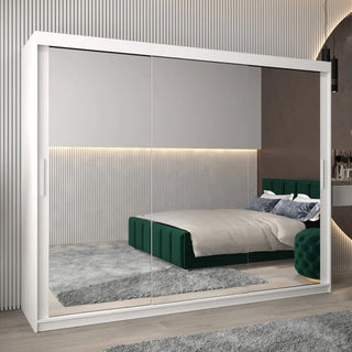 A modern bedroom with the CHOICEWARDROBE Tavira White High Gloss Mirrored Sliding Wardrobe (250cm, 3 doors), reflecting a green upholstered bed, gray rug, and a subtly lit wall with vertical grooves for stylish storage.