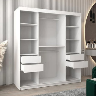The CHOICEWARDROBE Tavira White Mirrored Sliding Wardrobe (180cm, 2 Door) with shelves, drawers, and hanging rail stands in a modern room with a striped wall, large round mirror, and a partially visible green chair.