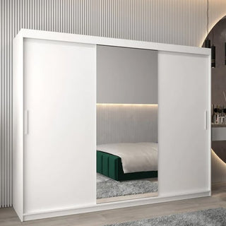 The CHOICEWARDROBE Tavira White Mirrored Sliding Wardrobe (250cm, 3 doors) features a full-length mirror, shelves, and hanging rails. Its modern design adds elegance to the bedroom, reflecting a green bed and striped wall paneling.