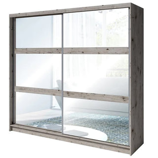 The CHOICEWARDROBE Terni 230cm Sliding Mirrored Wardrobe in Wellington Oak with glass panel doors stands in a bright room, its rustic finish adding charm while mirrors reflect a sofa, window, and rug—ideal for modern bedroom storage.