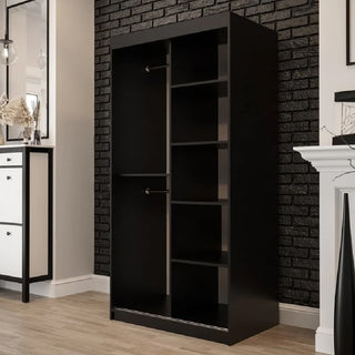 The CHOICEWARDROBE Topeka 100cm Dark Oak & Black Sliding Mirrored Wardrobe, with a modern industrial design, stands against a black brick wall. The room has light wood floors, a white fireplace, and a mirrored white cabinet with dried flowers.