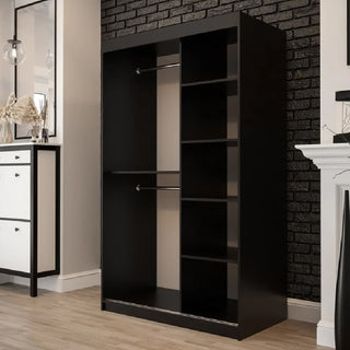 The CHOICEWARDROBE Topeka 120cm Dark Oak & Black Sliding Wooden Wardrobe, featuring two hanging rods and five shelves, stands against a black brick wall in a light wood-floored room with a white cabinet and decor nearby.