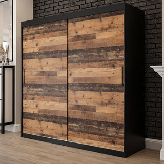The CHOICEWARDROBE Topeka 2 Door Sliding Wardrobe (200 cm) in dark oak and black finish, featuring industrial wooden design with shelves and hanging rails, stands stylishly against a black brick wall on wooden flooring.