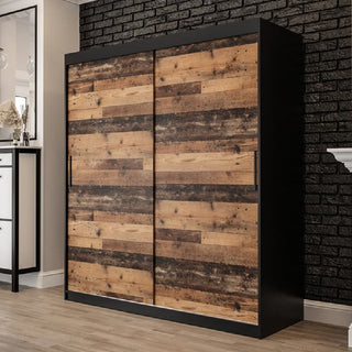 The CHOICEWARDROBE Topeka 180cm sliding door wardrobe in rustic oak and black stands on a light wood floor against a black brick wall, adding industrial style and modern storage to this room.