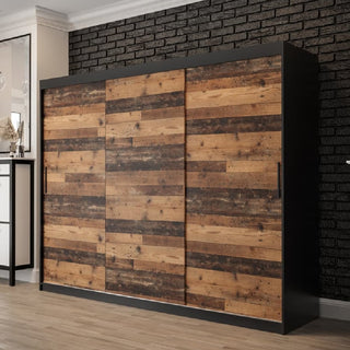The CHOICEWARDROBE Topeka Wooden Wardrobe, 250cm wide with 3 sliding doors in rustic oak and black finish, features ample shelving and dual hanging rails. It stands against a black brick wall on a light wood floor in an industrial loft style setting.