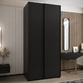 The CHOICEWARDROBE Tressaro Black Sliding Wardrobe – 2 Door (100cm wide, minimalist matte finish) adds sleek storage to a modern bedroom with light walls, wood paneling, and a small desk—ideal for contemporary spaces.