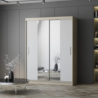 The CHOICEWARDROBE Vetra 2 Door Sliding Mirror Wardrobe (150cm, matt white with Sonoma oak trim) stands against a gray wall. A low round table with a vase and twigs is in front, with shelves built into the right side.